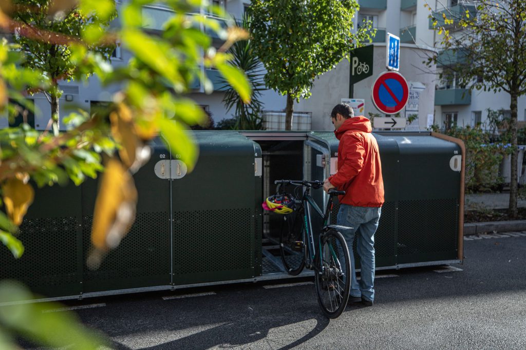 cycliste en train de déposer son vélo dans le parking vélos Filao avec un arbre en premier plan